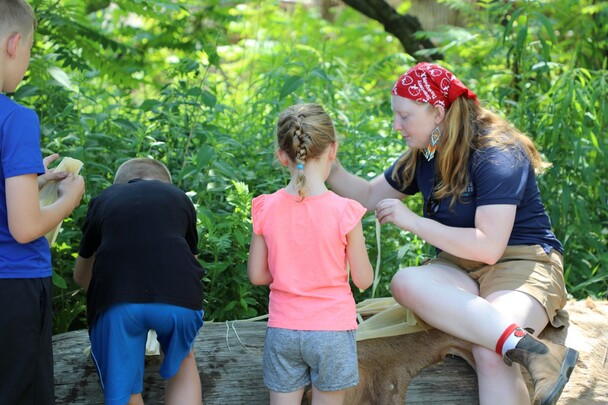 Museum educator instructs young guests on how to make a corn husk doll on the Homesite.