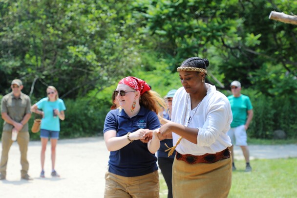 Two Educators on the Historic Patuxet Homesite hold hands and demonstrate a Wampanoag dance