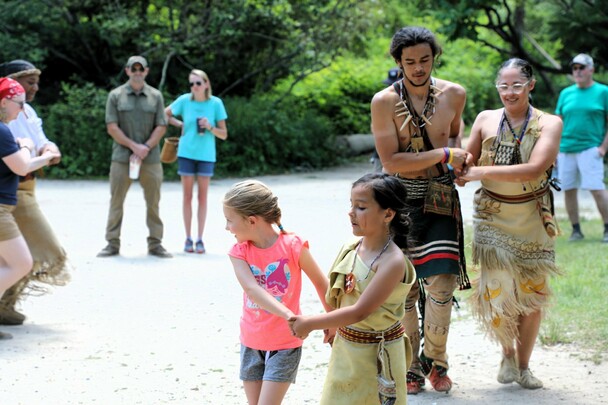 Educators and guests hold hands in pairs as they participate in a Wampanoag dance on the Historic Patuxet Homesite