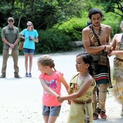 Educators and guests hold hands in pairs as they participate in a Wampanoag dance on the Historic Patuxet Homesite